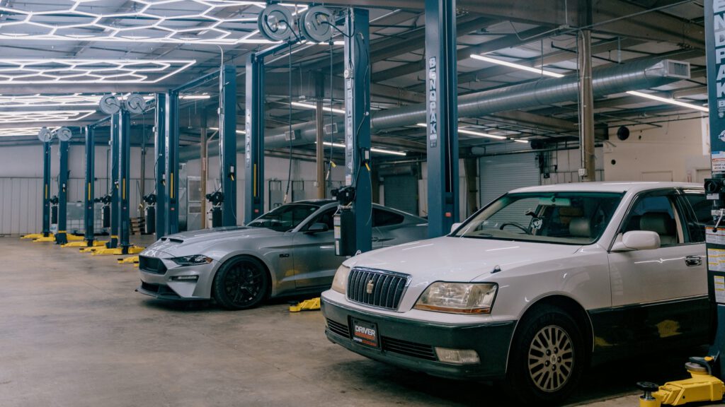 Two cars parked under BendPak two-post lifts, with a row of empty lifts behind them